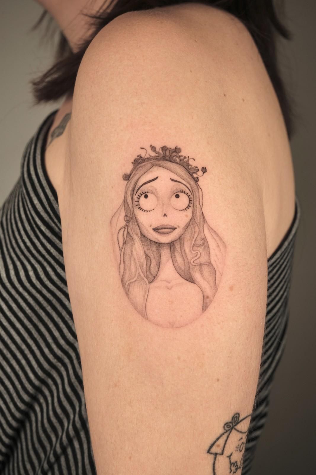 Tatuaje de Emily de La novia cadáver en la parte superior del brazo; ilustración en blanco y negro con expresión triste.