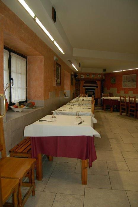 Comedor con mesas largas cubiertas con manteles blancos y una fila de sillas a lo largo de la pared.