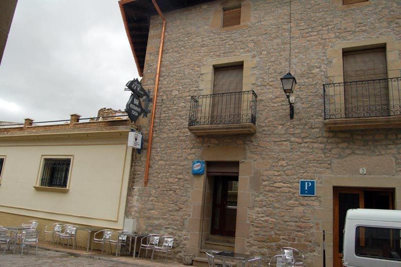 Fachada de un edificio de piedra en una calle estrecha, con balcones, una farola y una señal de aparcamiento azul.