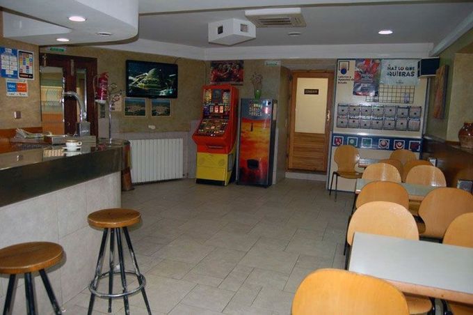 Cafetería vacía con mesas, taburetes, máquinas expendedoras y suelo de baldosas bajo luces fluorescentes.