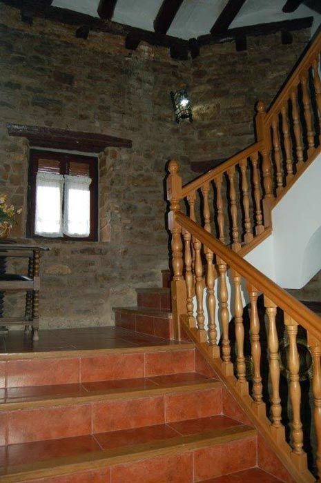 Escalera de piedra con barandilla de madera, ventana pequeña y paredes de ladrillo visto.