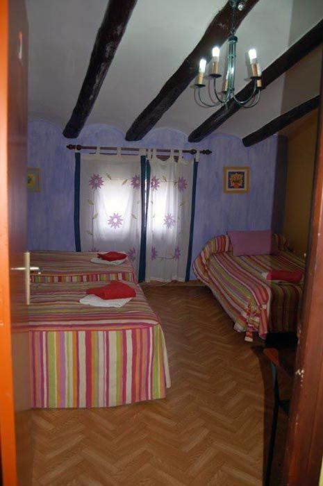 Habitación pequeña con dos camas individuales, colchas a rayas, vigas de techo a la vista y una ventana con cortinas.