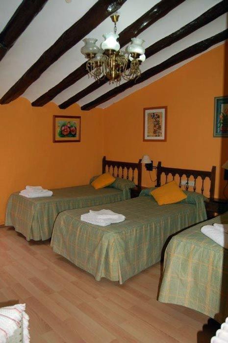 Acogedora habitación con tres camas individuales, colchas verdes, paredes naranjas y vigas de madera a la vista en el techo.
