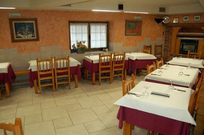 Comedor vacío de un restaurante con mesas puestas, manteles blancos y sillas de madera bajo una iluminación cálida.