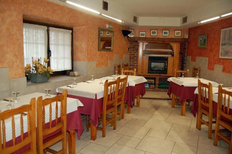 Comedor vacío de un restaurante con mesas cubiertas con manteles blancos, sillas de madera, detalles en rojo y una chimenea.