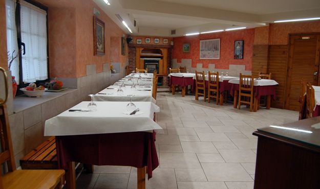 Comedor vacío de un restaurante con mesas puestas, suelo de baldosas blancas y paredes de color naranja cálido.