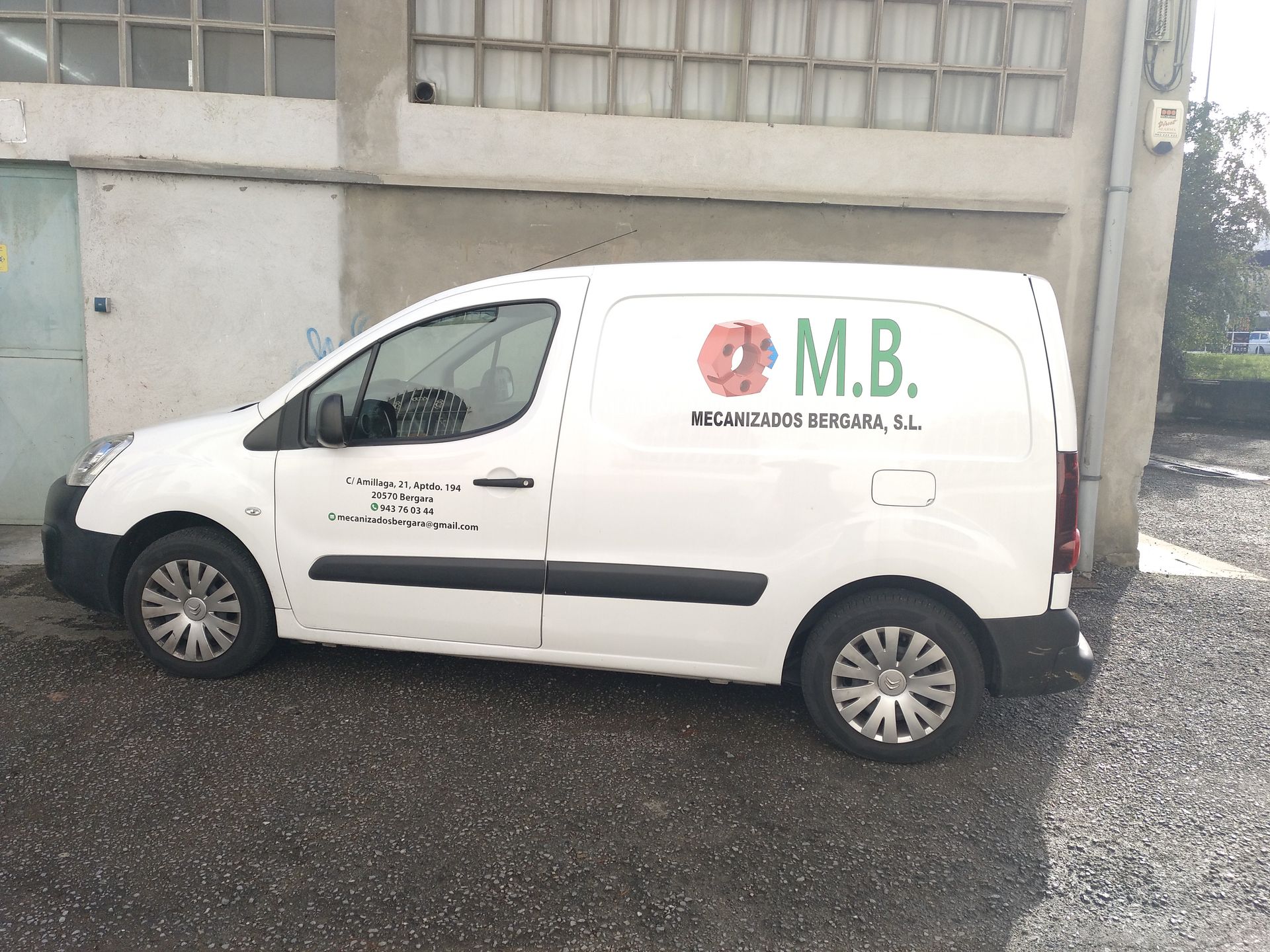 Una furgoneta MB blanca está estacionada frente a un edificio.