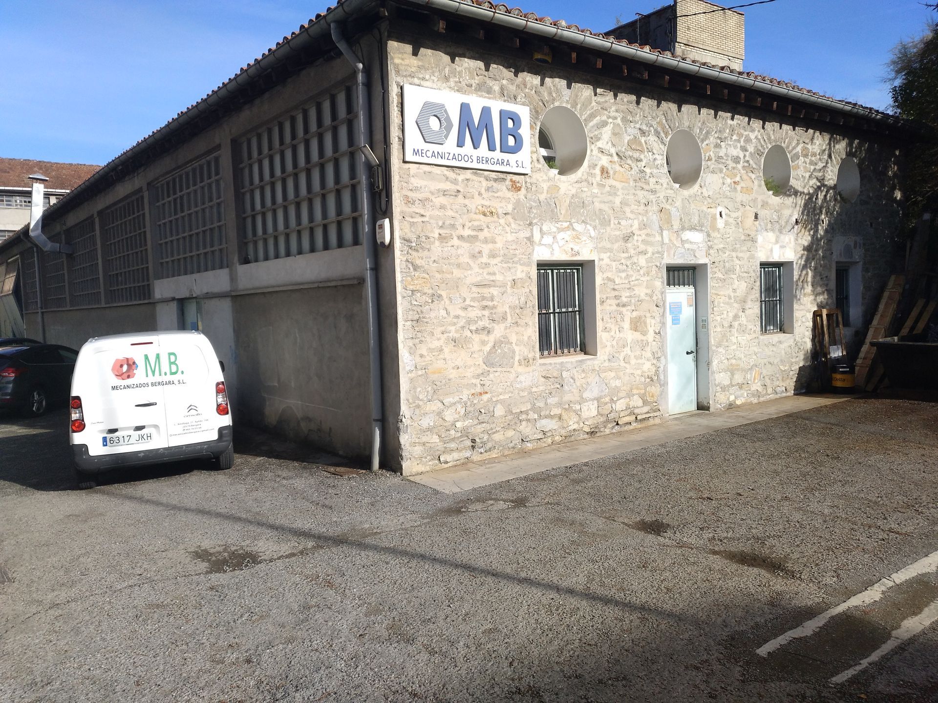 Una furgoneta MB blanca está estacionada frente a un edificio.