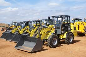 Una fila de tractores amarillos están estacionados en un campo de tierra.