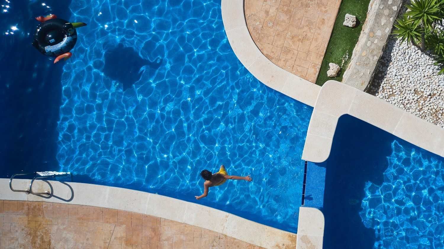 Vista aérea de una piscina con una persona nadando y un flotador cerca.