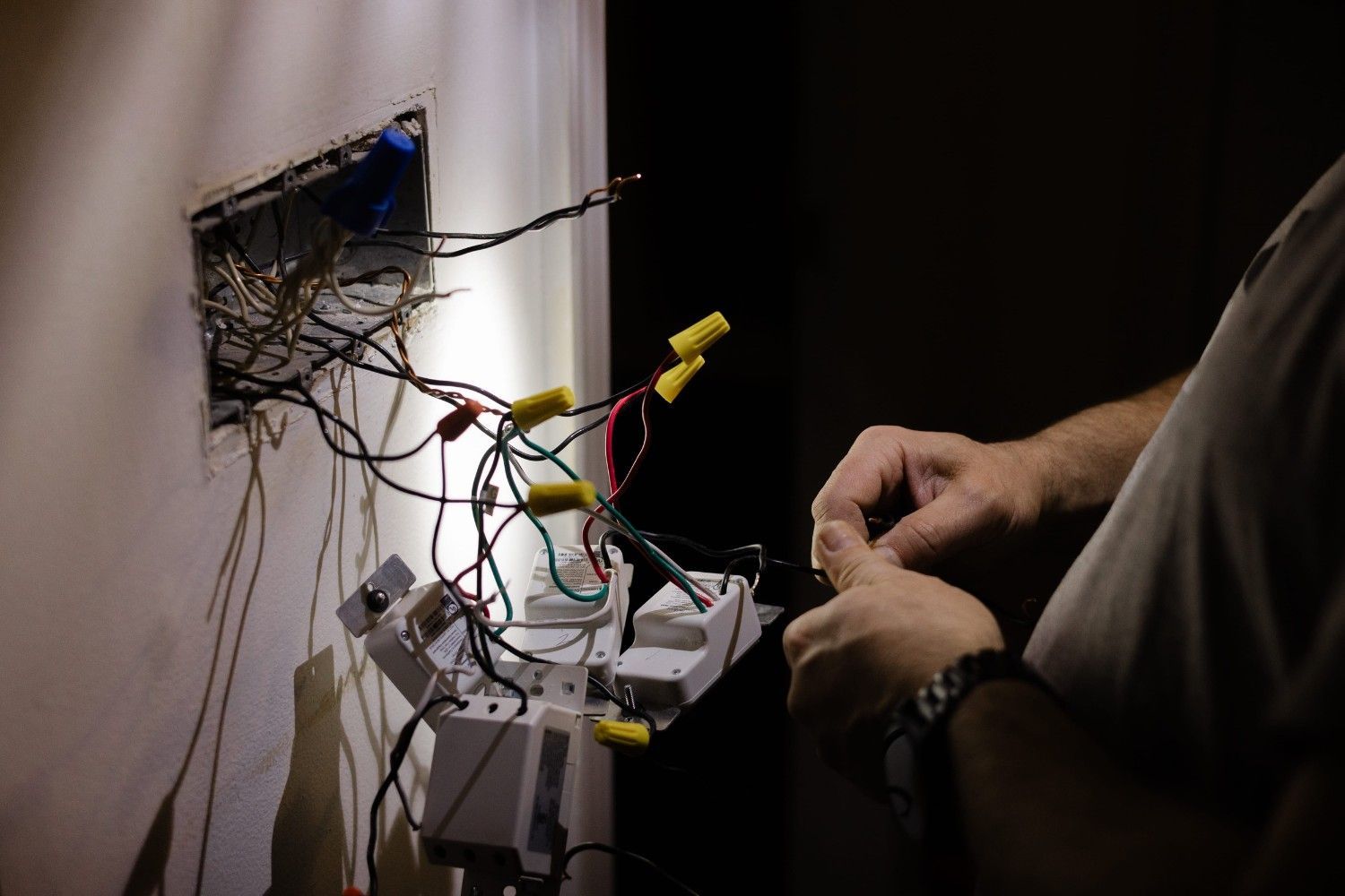 Las manos de una persona trabajando en el cableado eléctrico expuesto dentro de una caja de conexiones de pared.