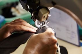 Hände nähen dunklen Stoff mit einer Nähmaschine. Nahaufnahme, Innenraum.