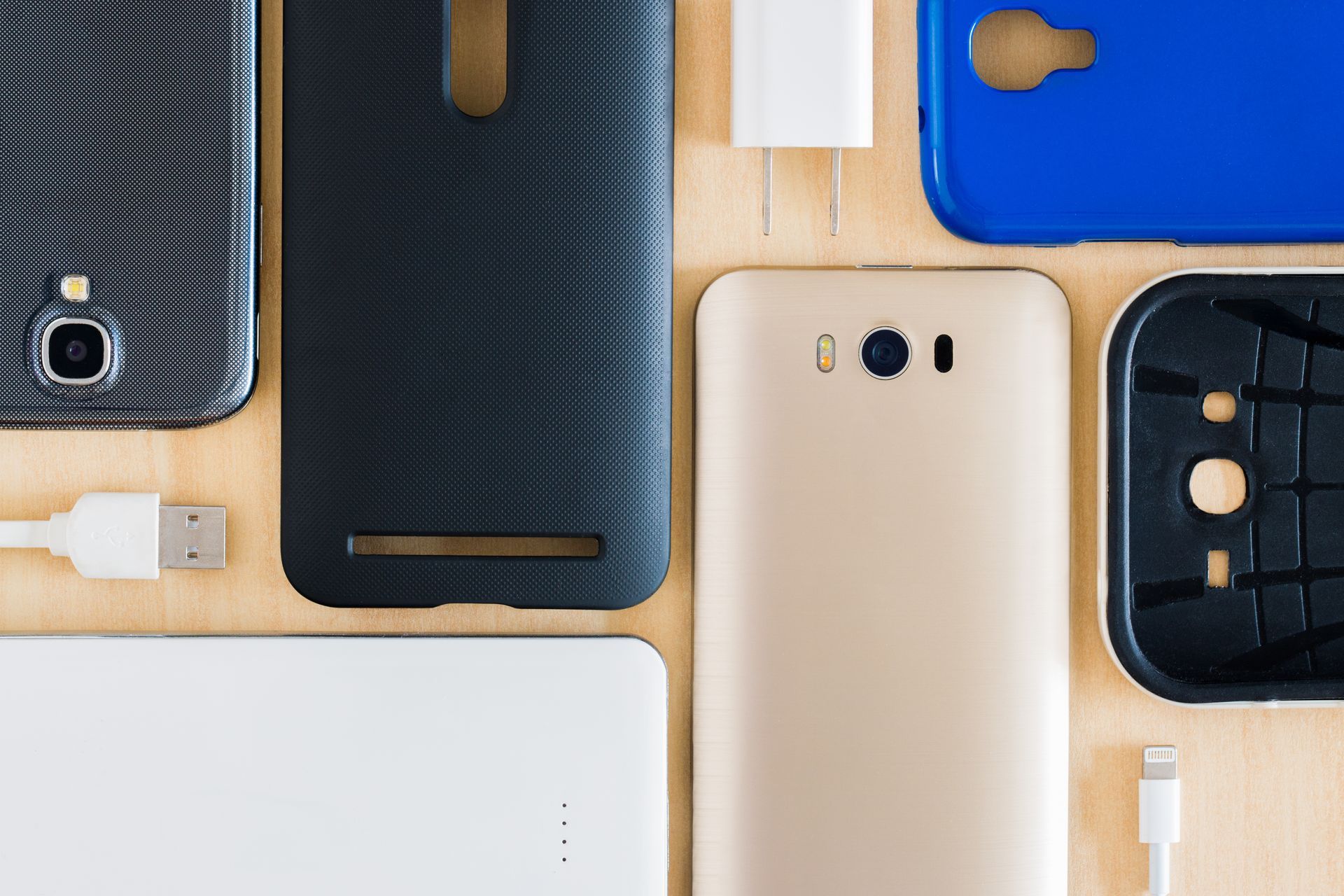 Étuis et coques arrière pour smartphones assortis, de couleur noire, beige et bleue, sur une surface en bois.