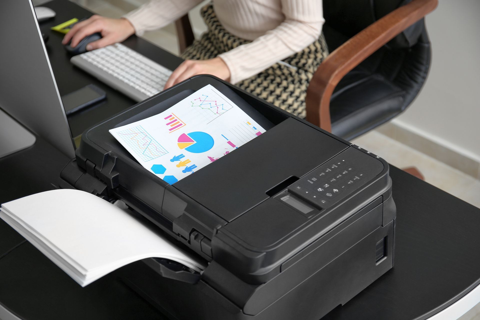 Imprimante/scanner de bureau imprimant un nuancier à côté d'une personne travaillant à un bureau.