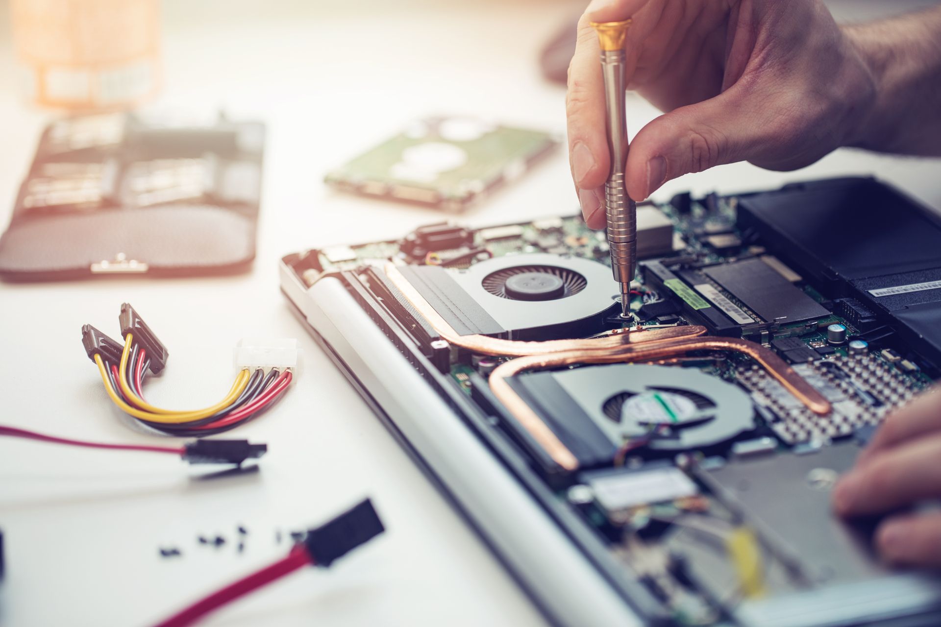 Des mains réparent un ordinateur portable ouvert, outils et composants internes visibles.