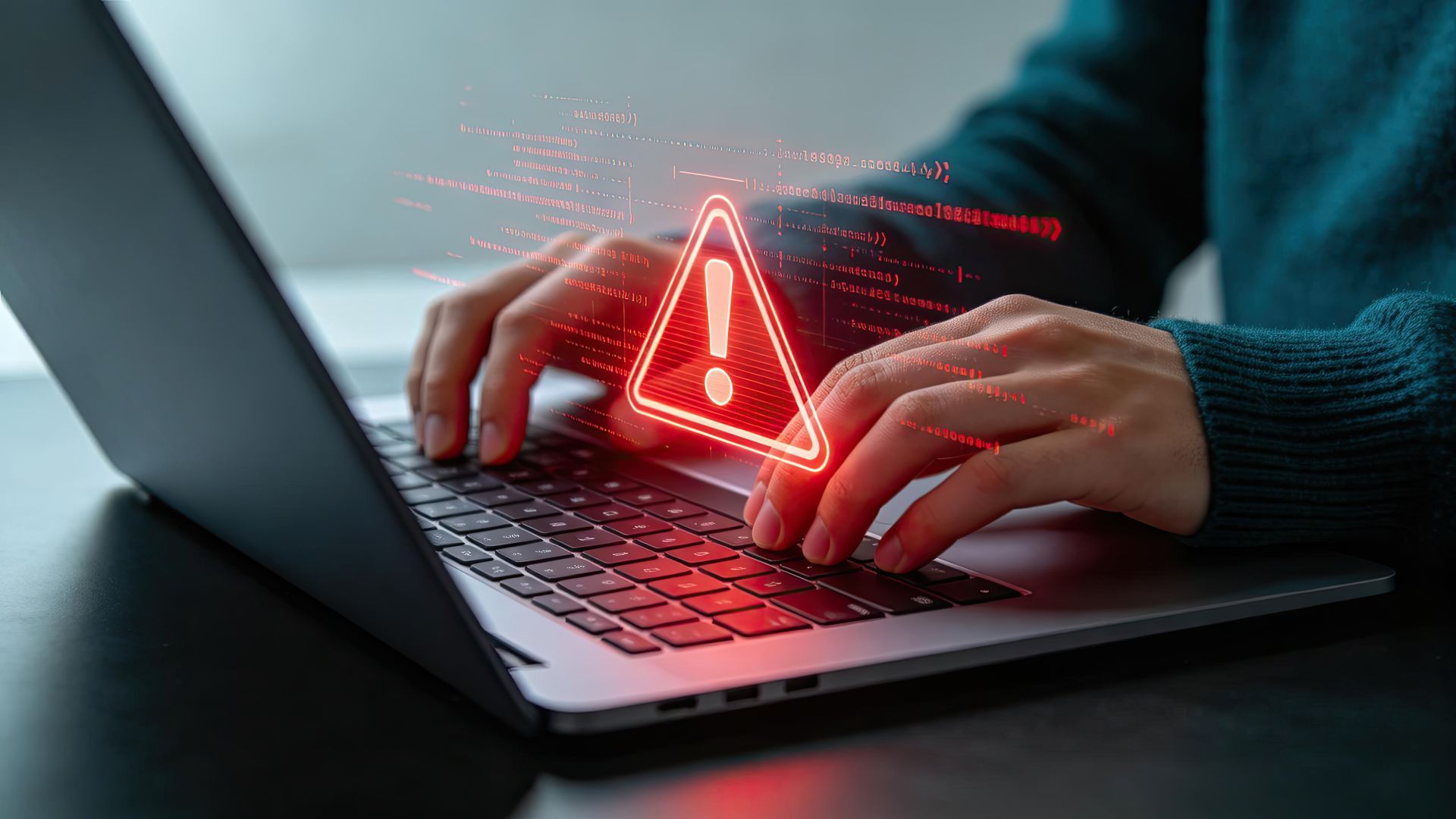 Des mains tapent sur un ordinateur portable avec un triangle d'avertissement rouge lumineux sur l'écran.
