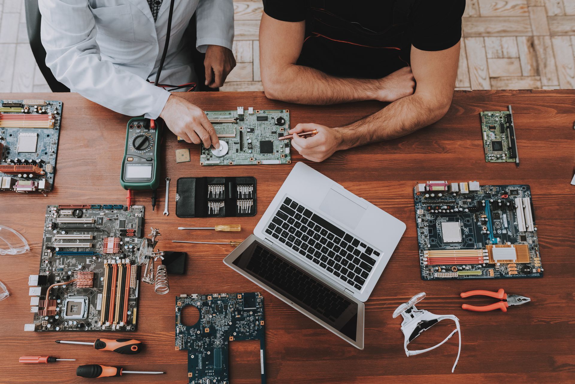 Des personnes et un ordinateur portable entourés de circuits imprimés et d'outils sur une table en bois.