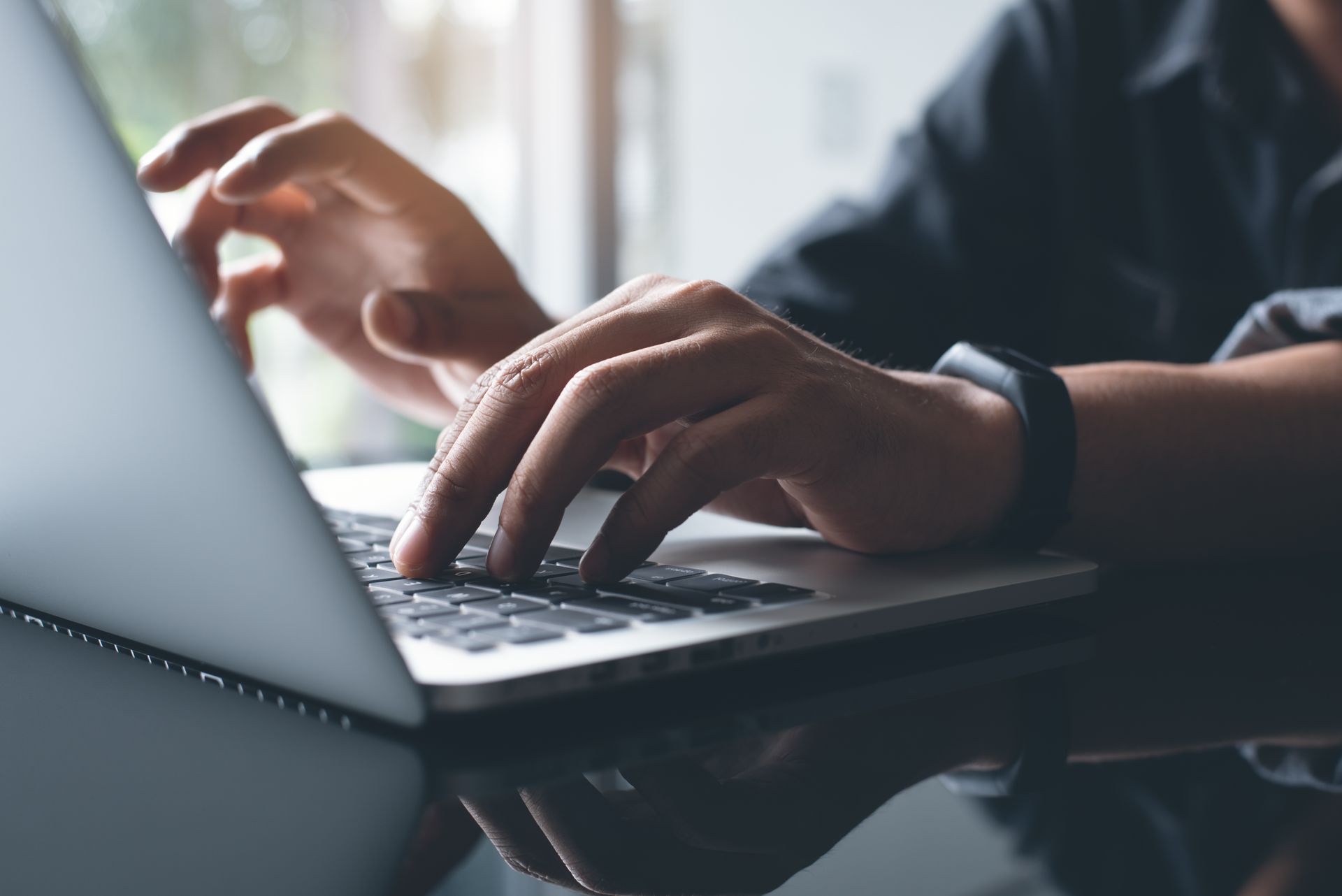 Des mains tapant sur le clavier d'un ordinateur portable à côté d'une tasse de café sur un bureau.