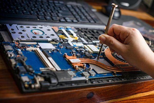 Une personne répare la carte mère d'un ordinateur portable avec un tournevis sur un bureau en bois.