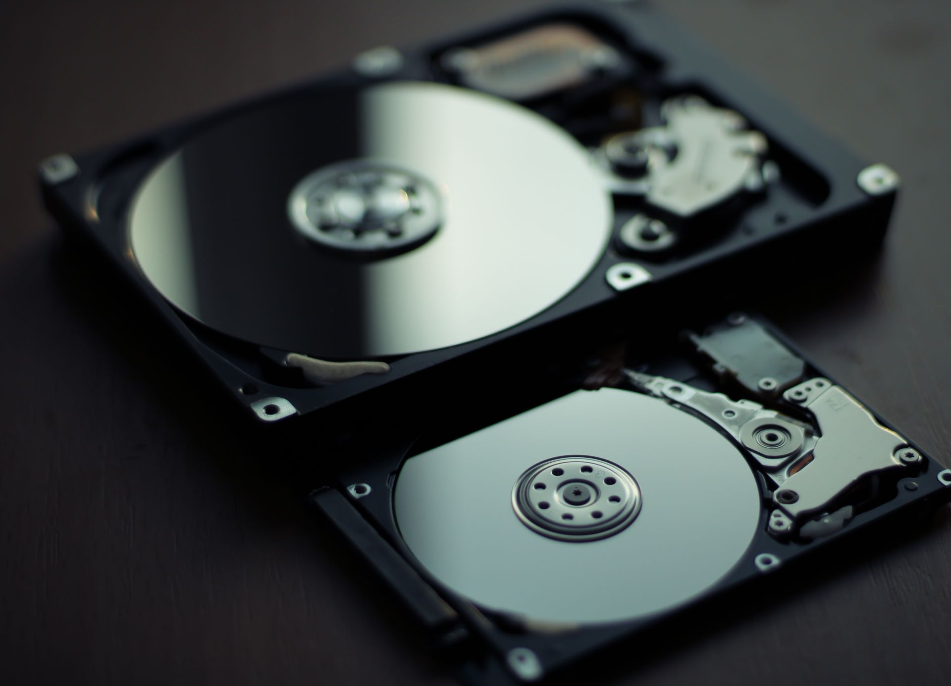 Deux disques durs ouverts sur une surface sombre, l'un d'eux avec un plateau argenté réfléchissant.