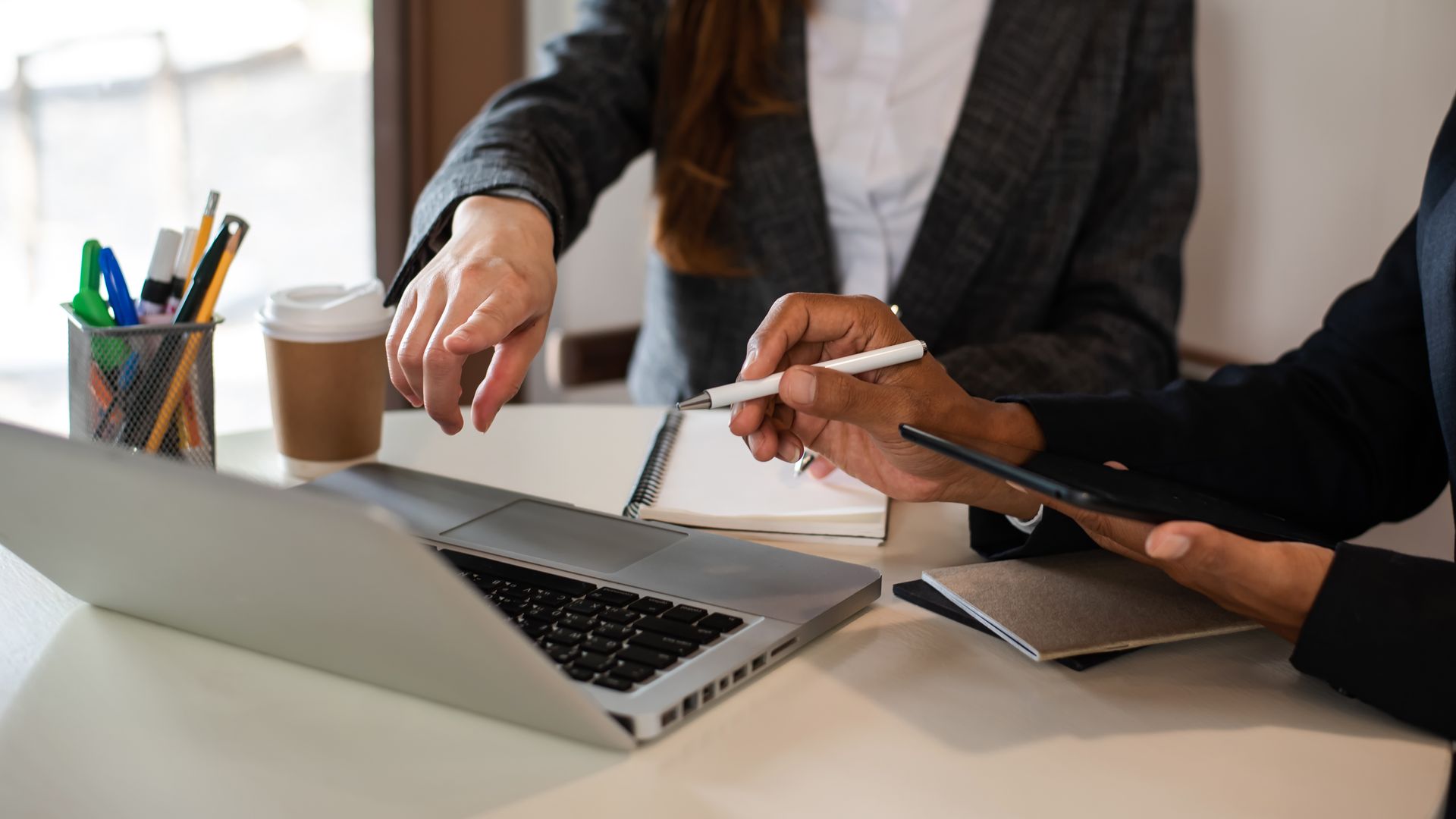 Deux personnes discutent d'un projet sur un ordinateur portable, l'une d'elles pointant du doigt une tablette posée sur un bureau.
