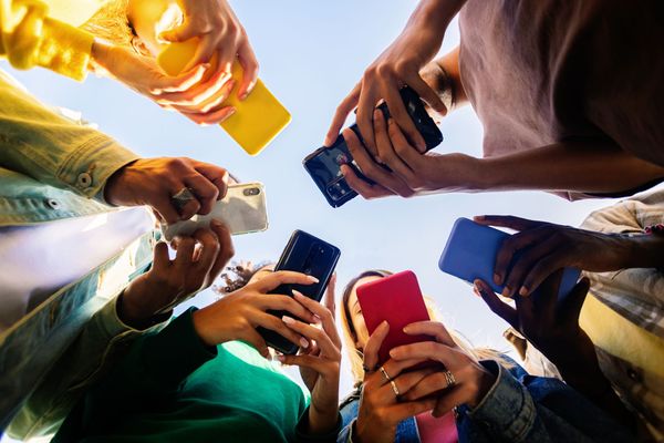 Des personnes tenant des smartphones en cercle, vues d'en bas sous un ciel lumineux.
