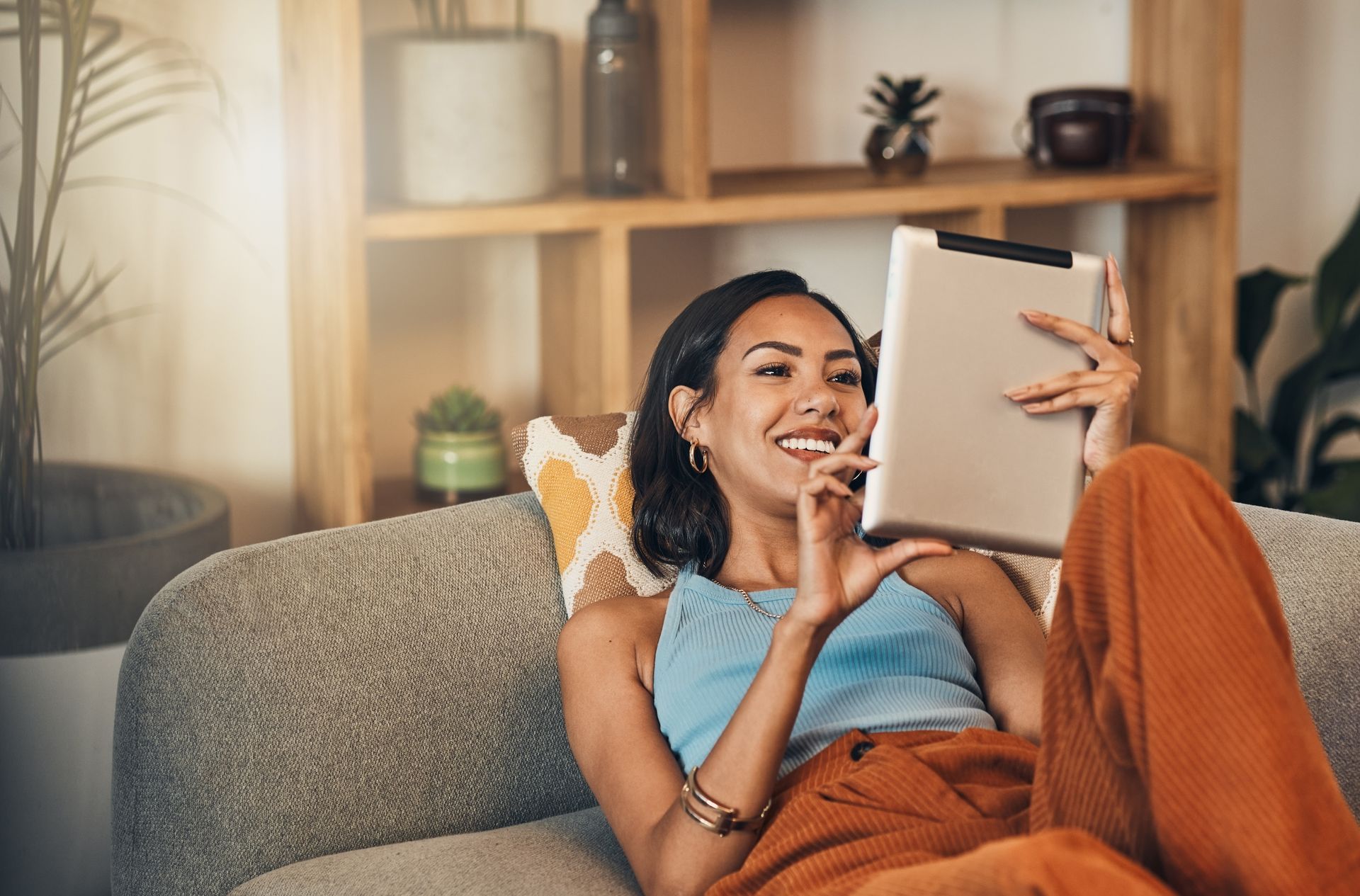 Une personne se détend sur un canapé, souriant en lisant une tablette dans un salon confortable.