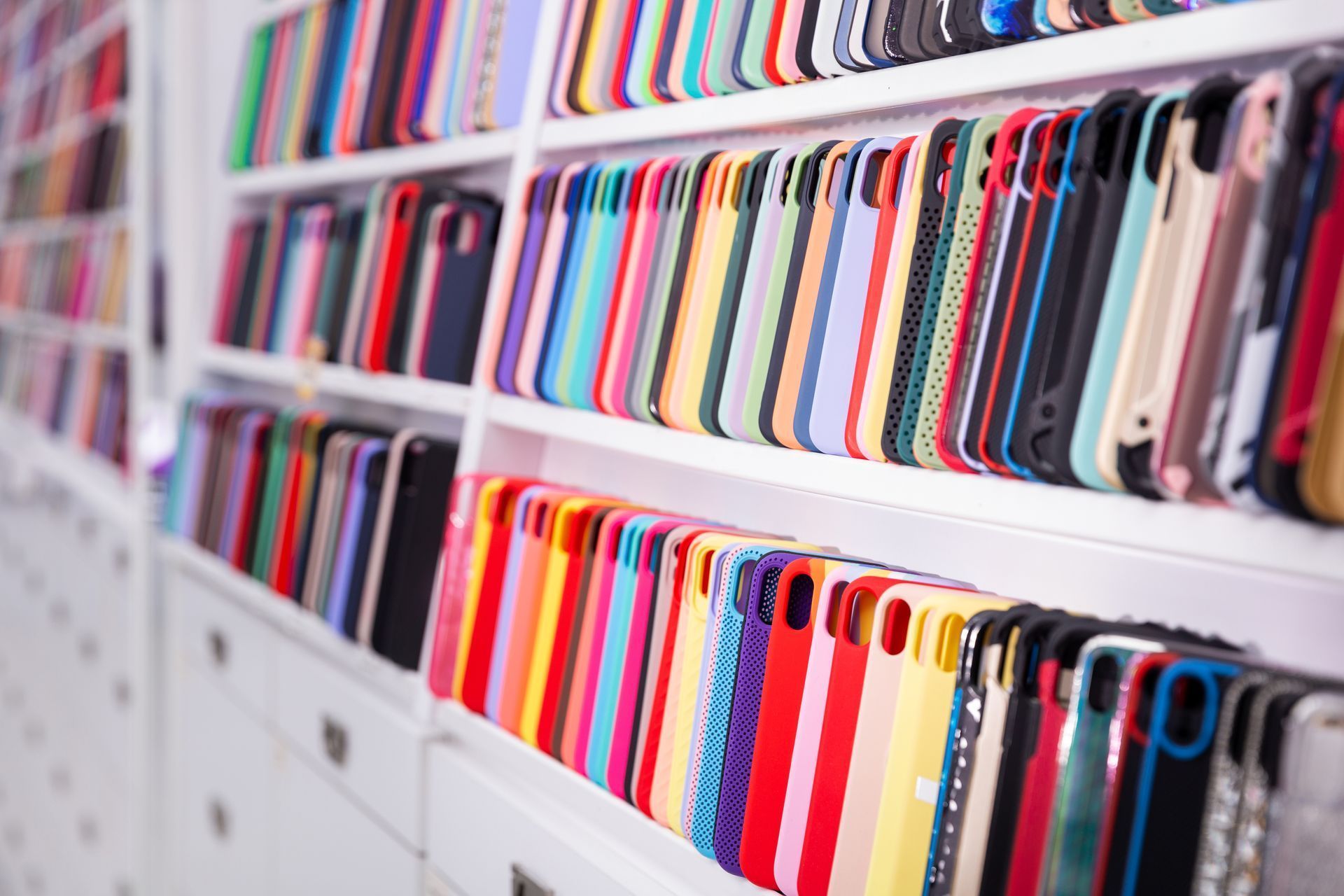 Des rangées de coques de téléphone colorées sont exposées sur des étagères blanches dans un magasin.
