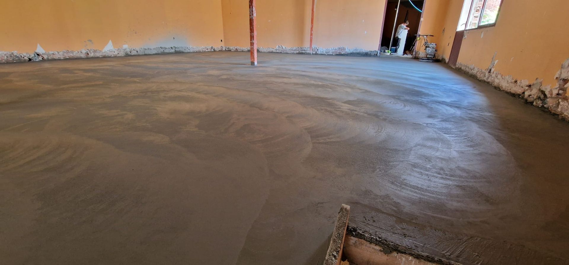 Una habitación con suelo de cemento liso y recién vertido. Las paredes son de color naranja pálido.