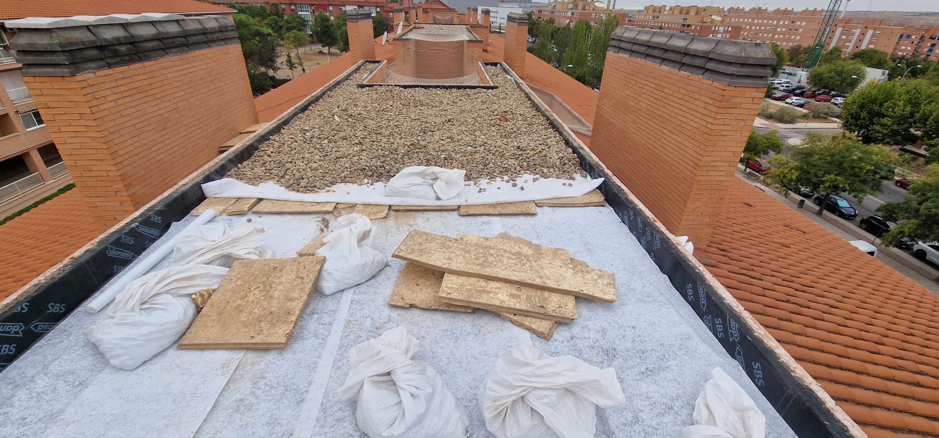 Azotea en construcción con materiales, ladrillos, grava y lonas blancas.