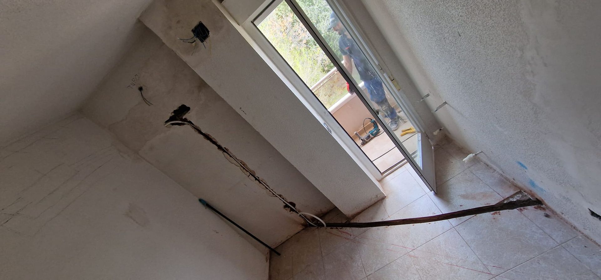 Fotografía interior de una habitación con una ventana, cables y grietas en el techo.