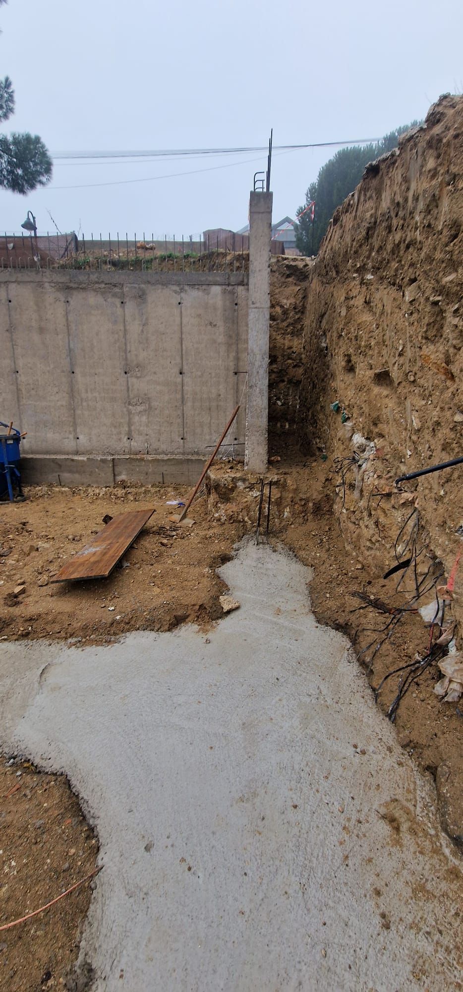 Obra con cimientos de hormigón y muro de contención. Tierra excavada y cielo nublado.