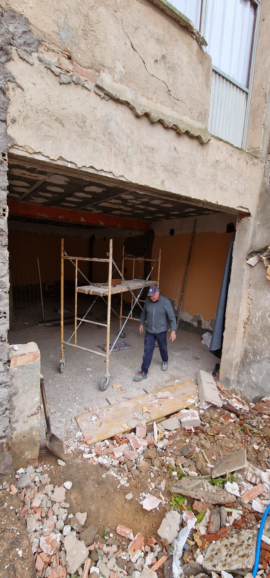 Hombre dentro de un edificio en construcción, de pie cerca de un andamio. Las paredes exteriores están dañadas.