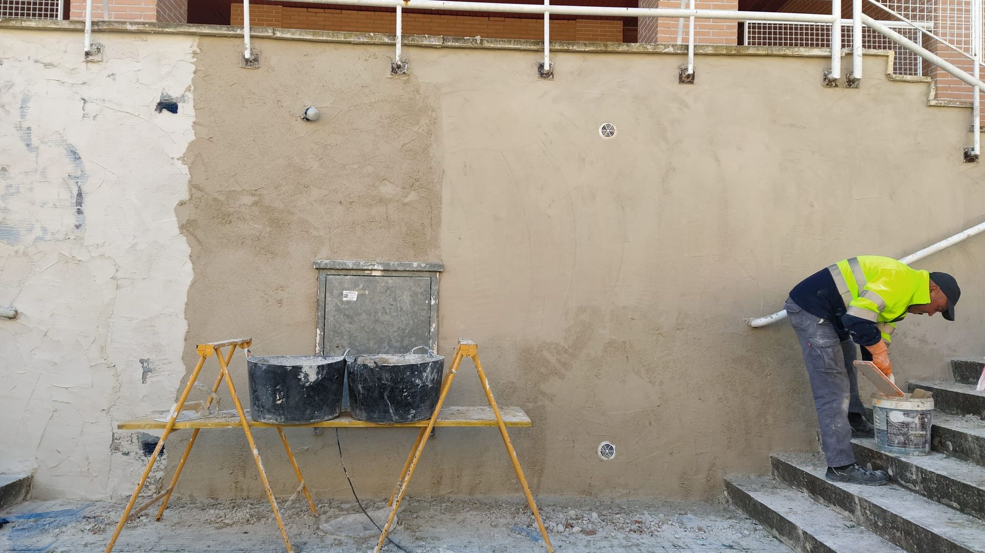 Un trabajador aplica yeso a una pared exterior. La pared tiene una sección parcialmente terminada.