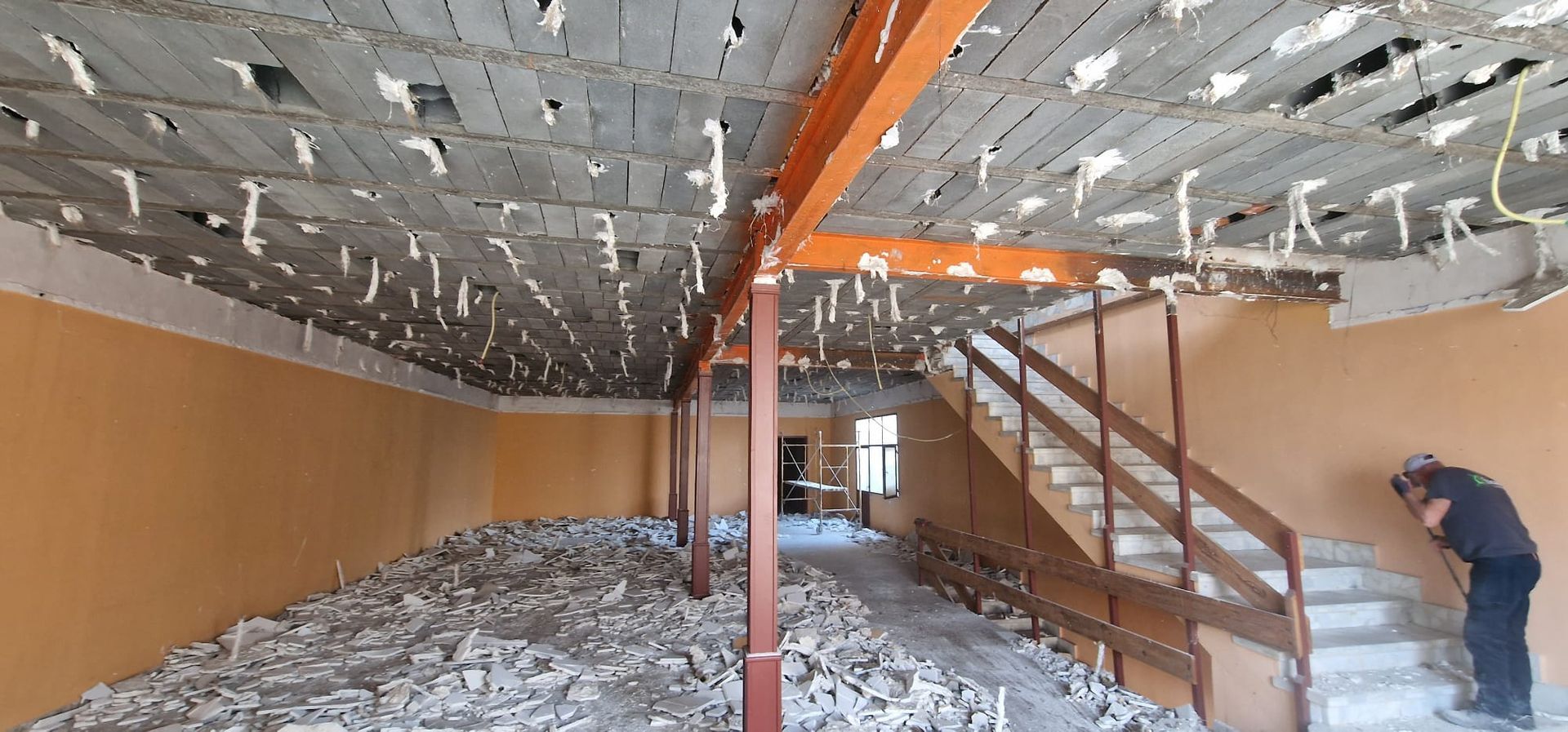 Interior de un edificio en remodelación con escombros en el piso y una persona mirando las escaleras.