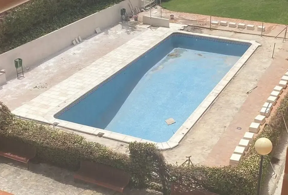 Edificio de ladrillo con ventanas blancas ornamentadas y balcón de hierro forjado. Ramas de árboles con flores blancas en primer plano.