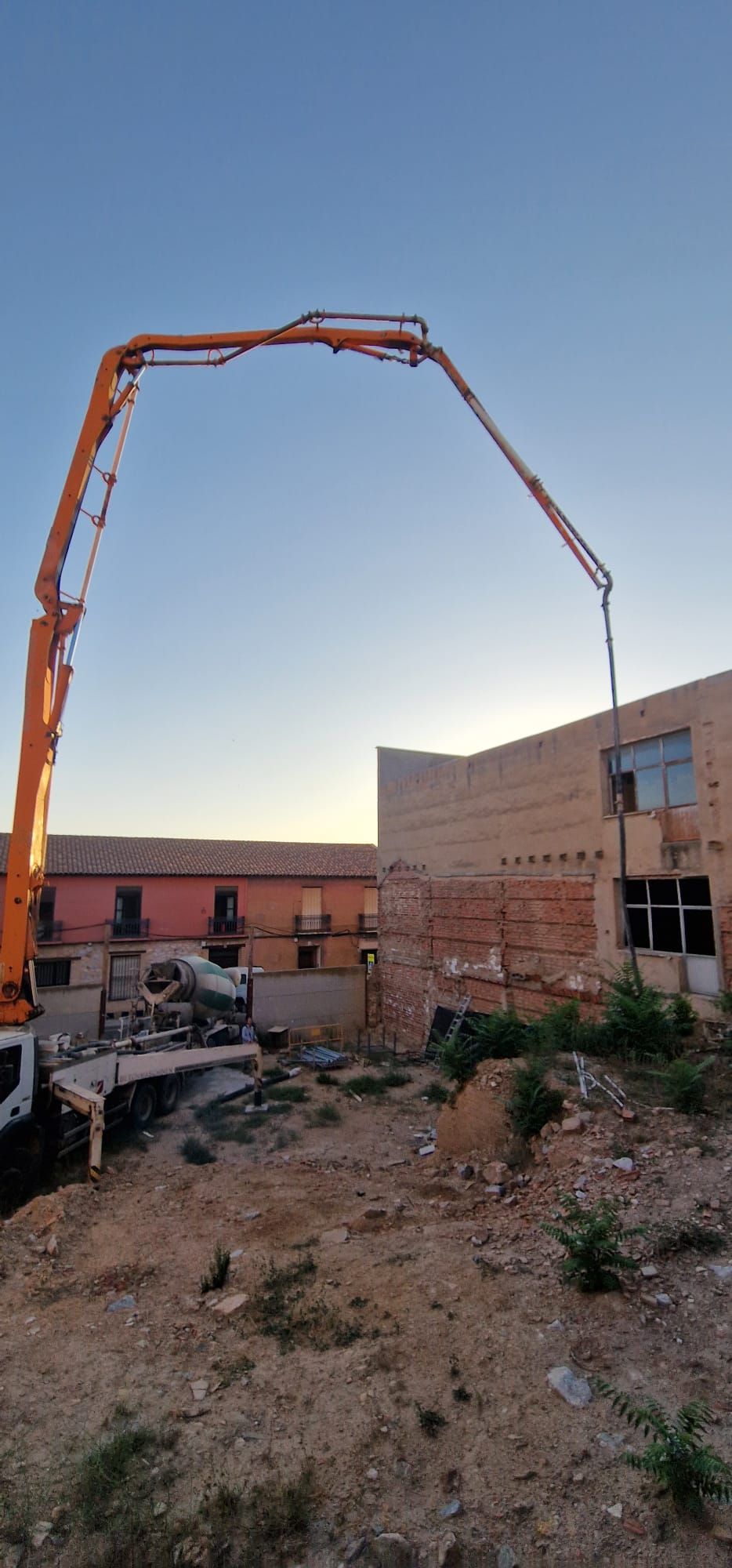 Un sitio de construcción con un camión bomba de hormigón que se extiende sobre un edificio.