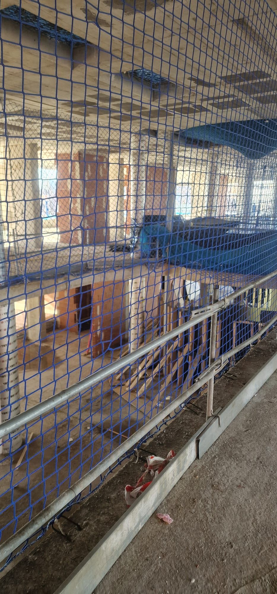 Una vista a través de una red de malla azul hacia el interior de un edificio, mostrando pasarelas de hormigón y comederos.