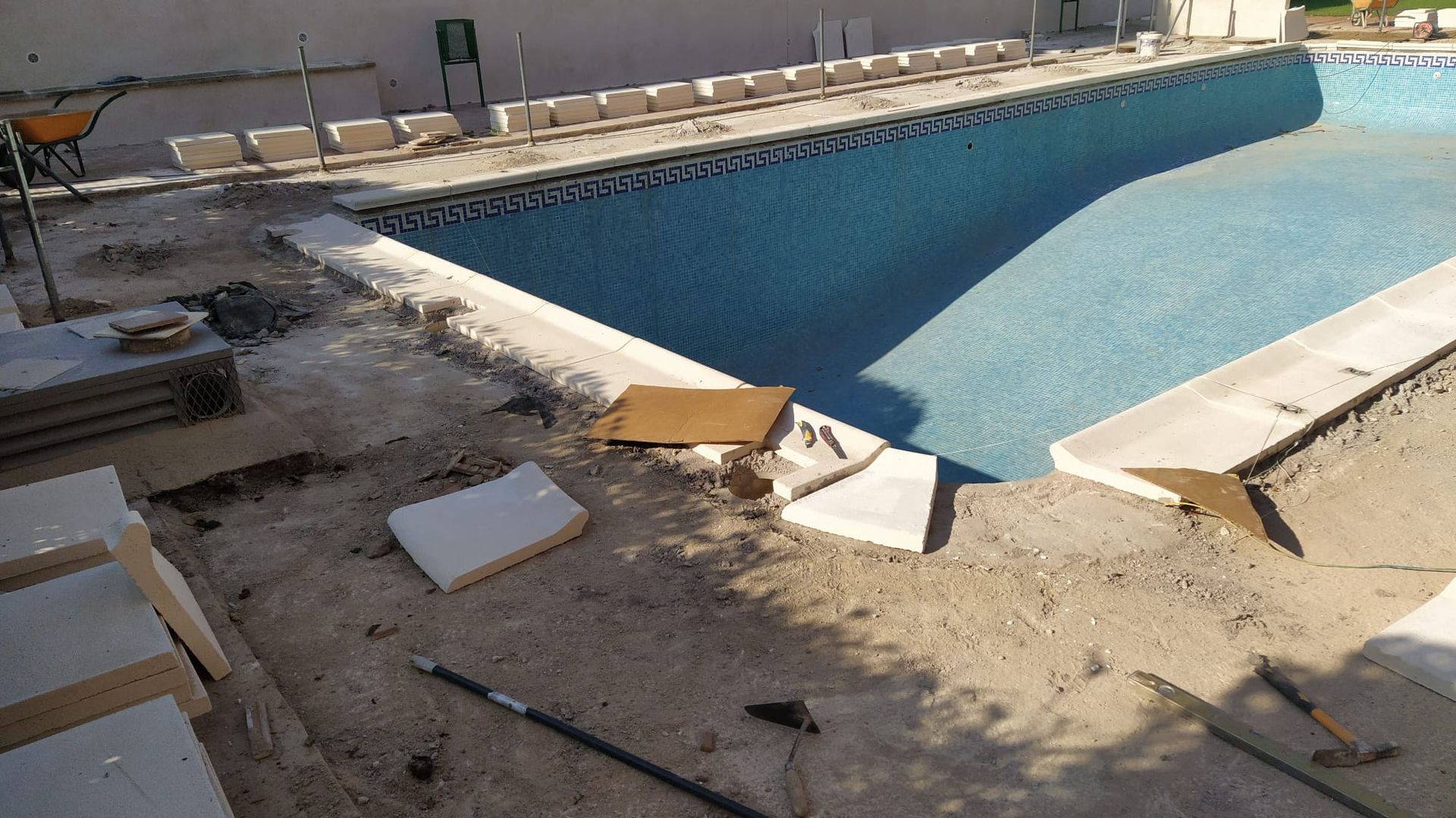 Piscina en construcción, con azulejos azules, piedras de coronamiento y escombros visibles.