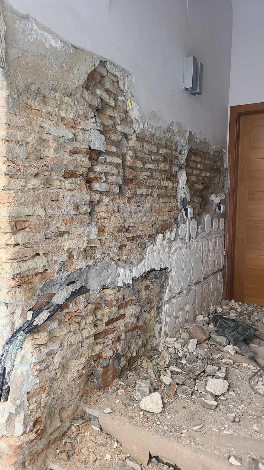 Muro parcialmente demolido, dejando al descubierto ladrillo y hormigón. Escombros en el suelo.