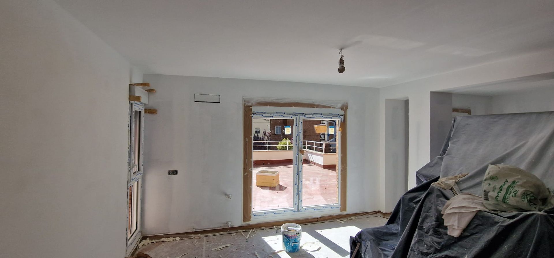 Interior de una habitación en construcción con paredes blancas, puerta y cubierta protectora.