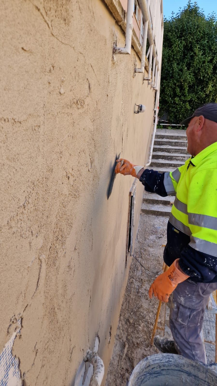 Hombre con chaleco de seguridad aplicando estuco a la pared de un edificio con una paleta.