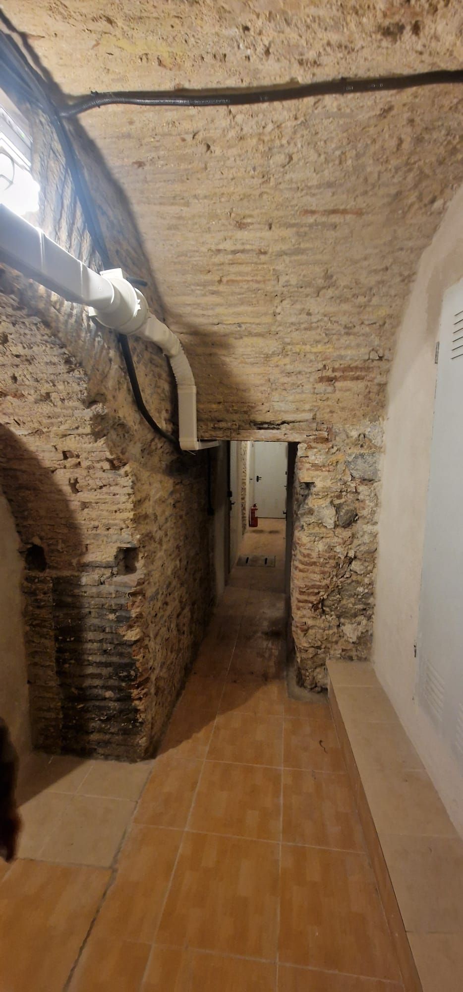 Pasillo estrecho con paredes de ladrillo, techo abovedado y suelo de baldosas.