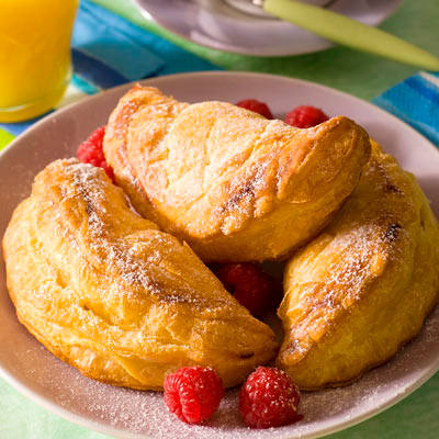 Trois pâtisseries dorées saupoudrées de sucre glace et garnies de framboises, disposées sur une assiette