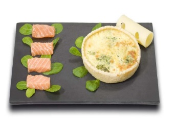 Quiche au saumon avec des morceaux de saumon et du fromage roulé, servie sur une assiette noire et garnie d'épinards.