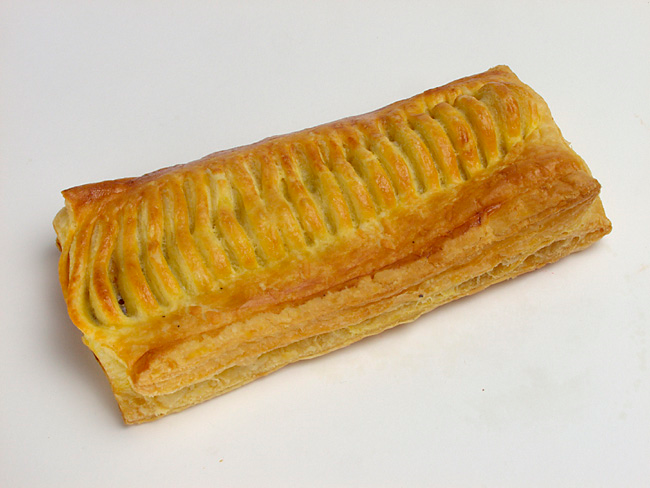 Rouleau de saucisse feuilleté et doré sur une surface blanche.