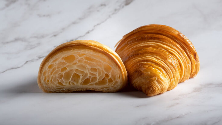 Deux croissants dorés posés sur une surface en marbre. L'un d'eux est tranché, révélant sa mie feuilletée.