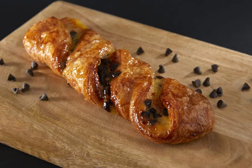 Pâtisserie torsadée aux pépites de chocolat sur une planche en bois.