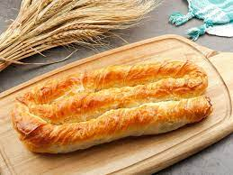 Pâtisserie roulée, dorée, sur une planche à découper en bois, avec des épis de blé en arrière-plan.