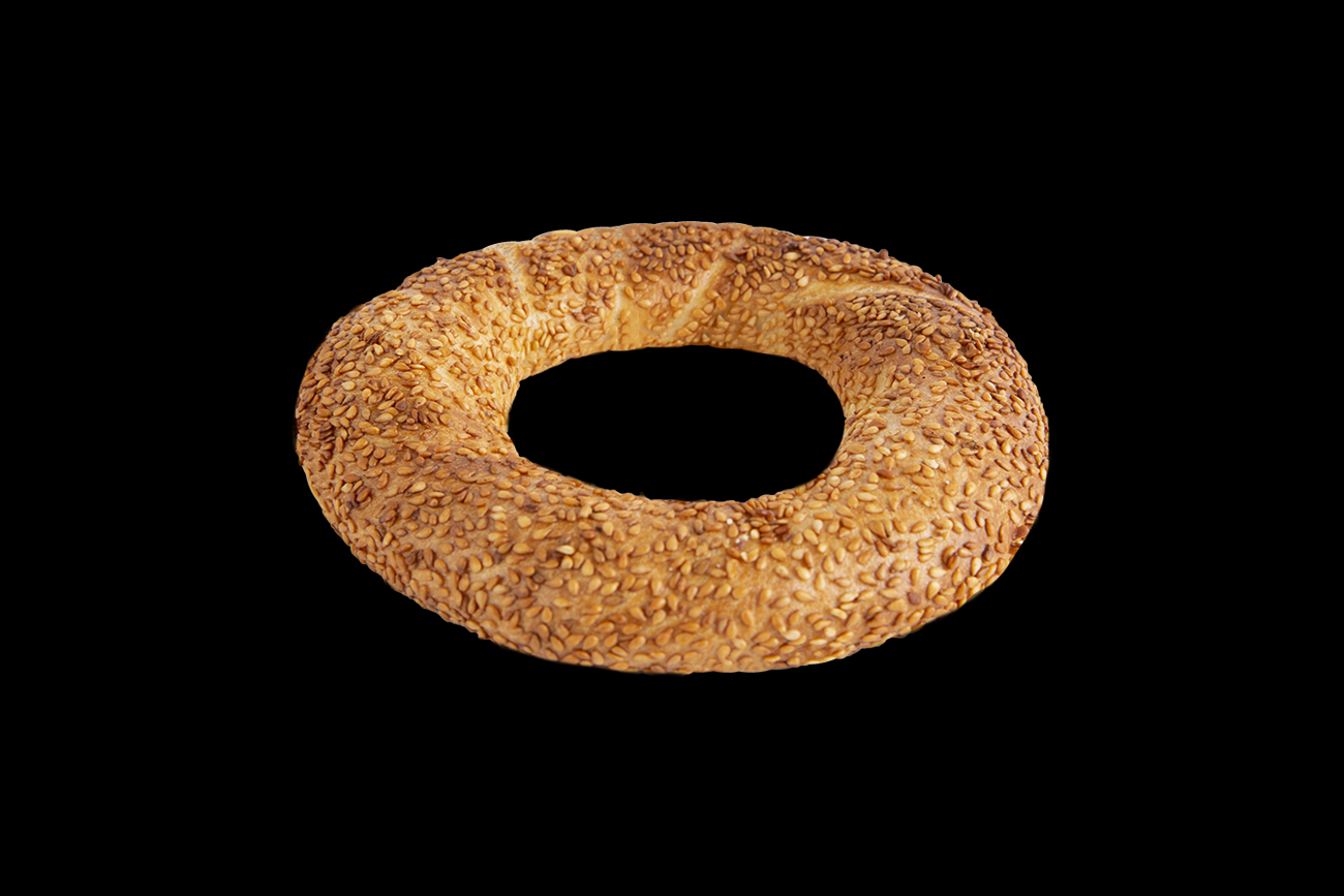 Pain rond recouvert de graines de sésame sur fond noir.